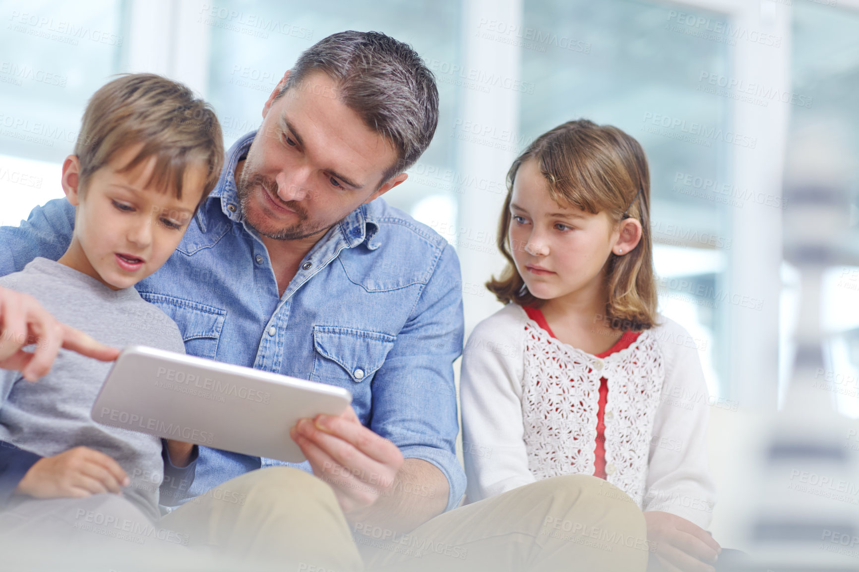 Buy stock photo Shot of a loving father using a digital tablet with his son and daughter at home