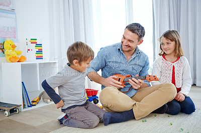 Buy stock photo Shot of a happy father playing the guitar for his son and daughter at home