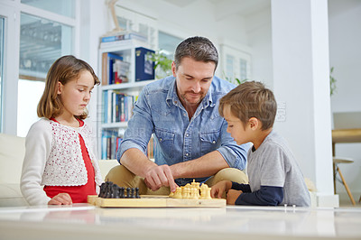 Buy stock photo Shot of a father playing a game of chess with his son and daughter at home