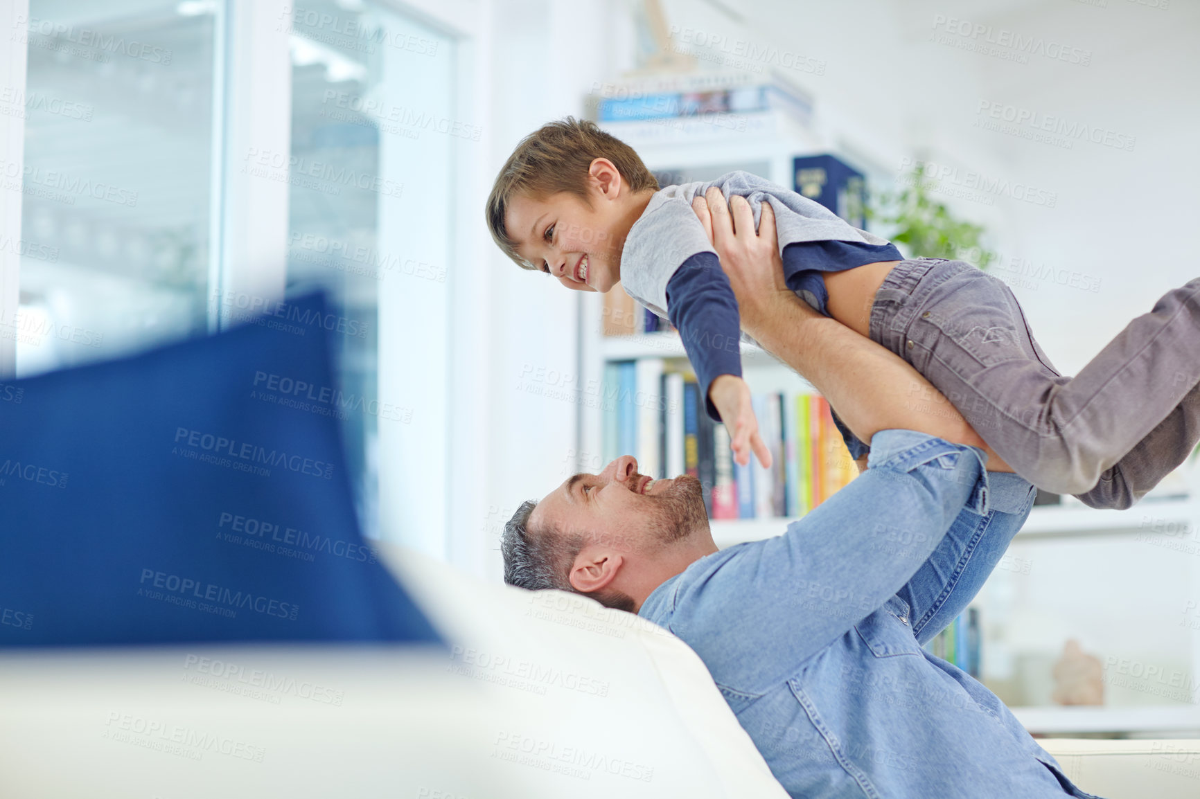 Buy stock photo Shot of a loving father sitting on the sofa while playfully lifting his son into the air