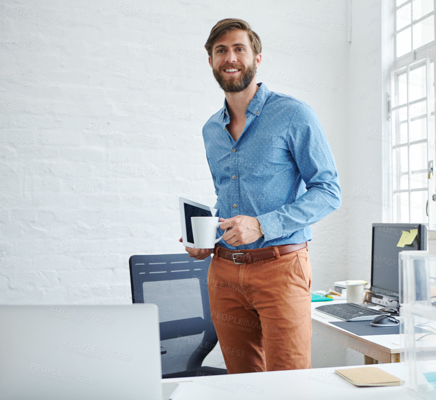 Buy stock photo Shot of a handsome designer holding a cup of coffee and a digital tablet