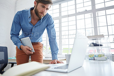 Buy stock photo A handsome designer holding his tablet while working on his laptop