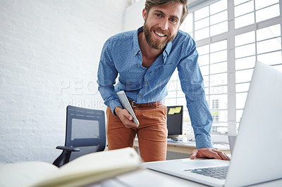Buy stock photo A handsome designer holding his tablet while working on his laptop
