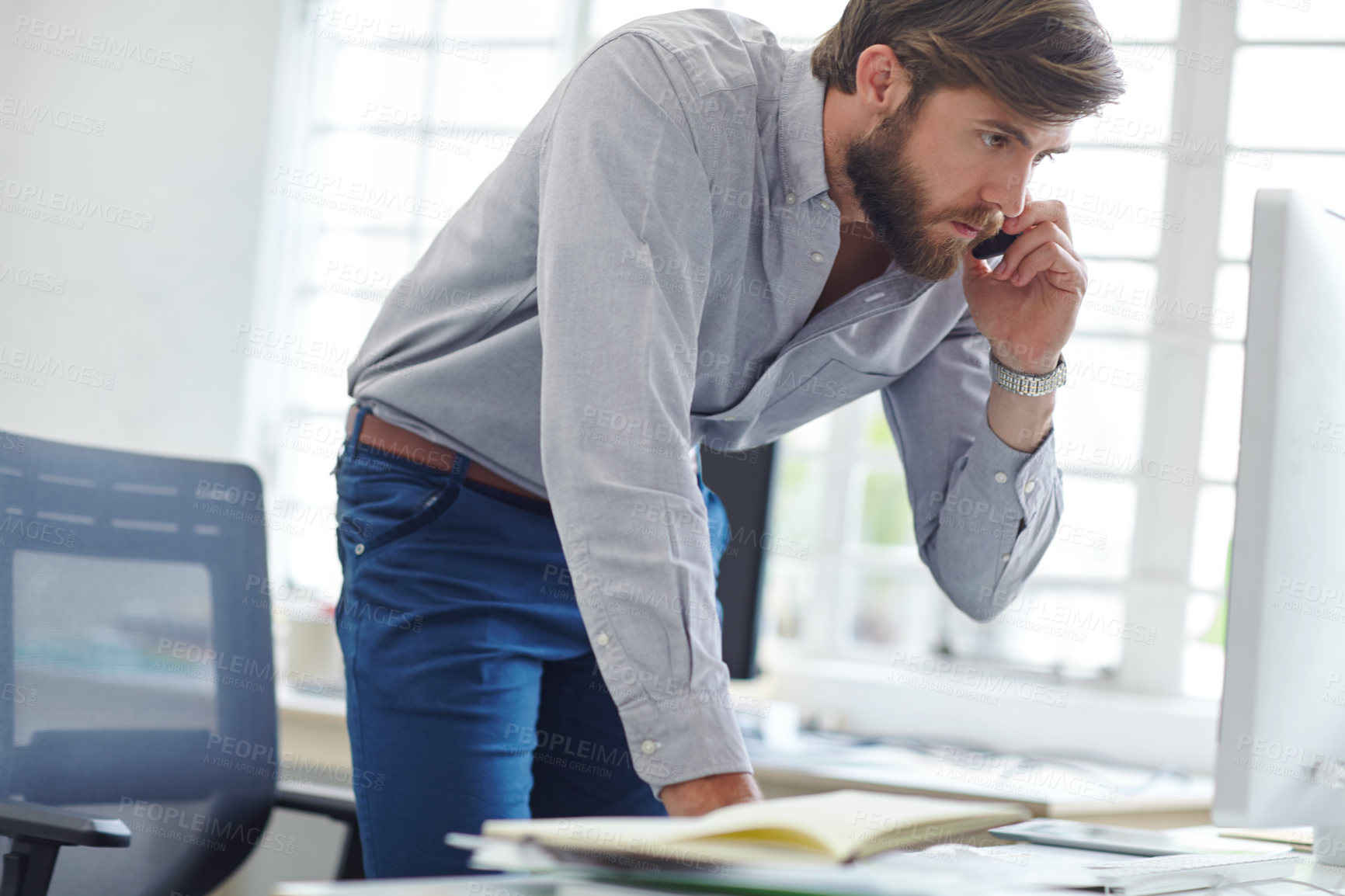 Buy stock photo Shot of a designer talking on his phone while reading something on his computer screen