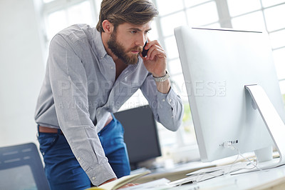 Buy stock photo Shot of a designer talking on his phone while reading something on his computer screen