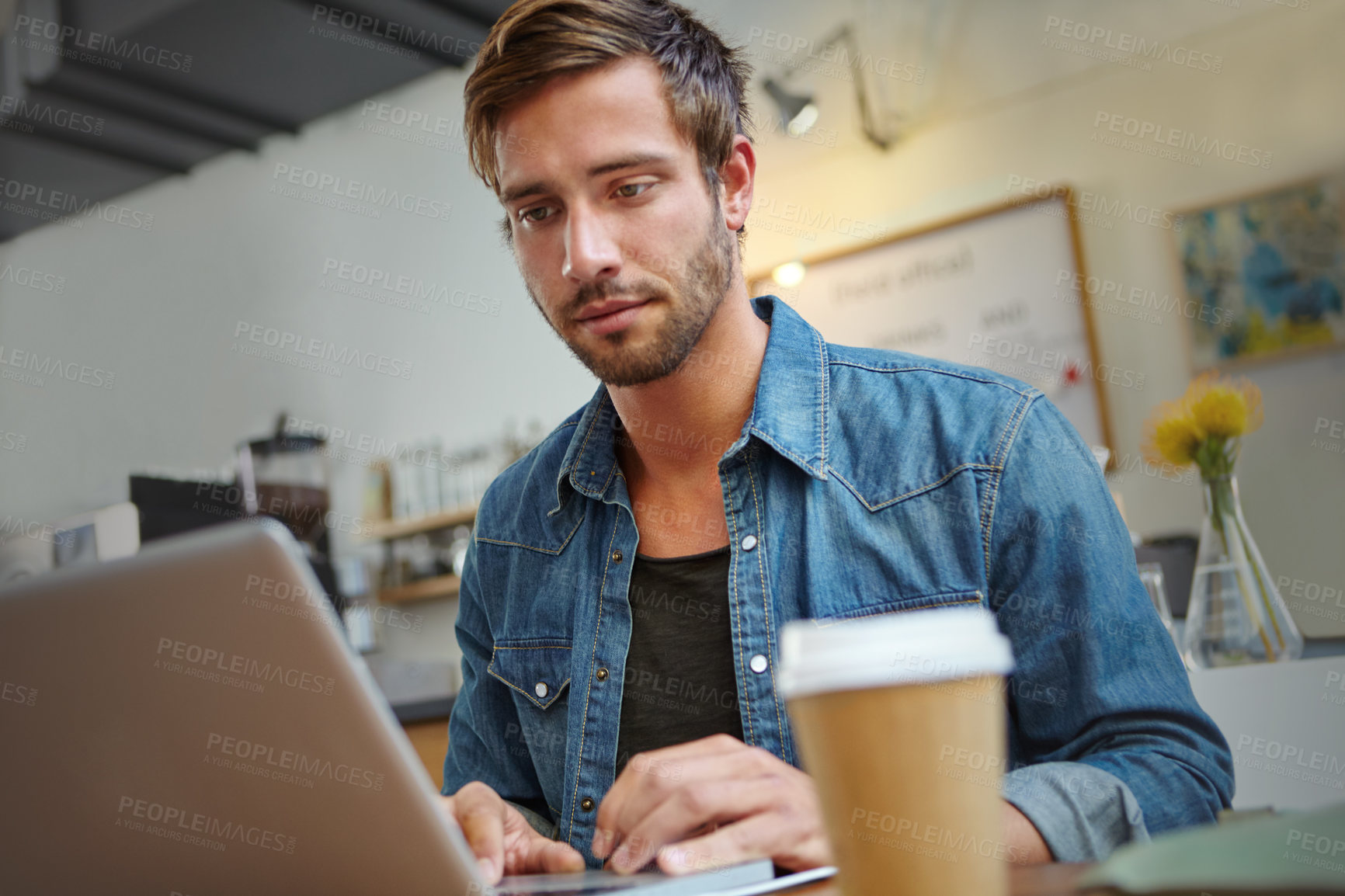 Buy stock photo Shot of a handsome young man working on his laptop in a coffee shop