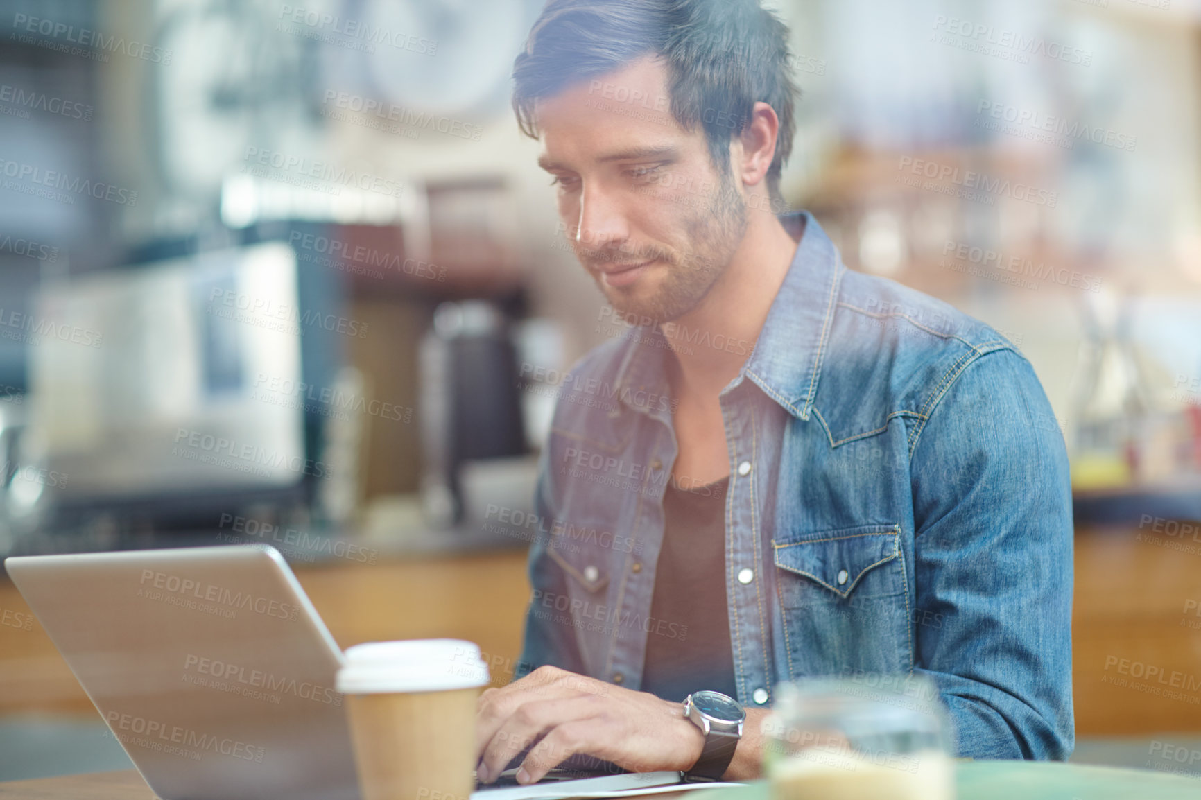 Buy stock photo Shot of a handsome young man working on his laptop in a coffee shop