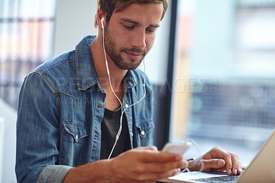 Buy stock photo Shot of a young man listening to music while using his laptop at a coffee shop