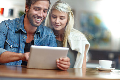 Buy stock photo Shot of a young couple looking at someting on a tablet while on a coffee date