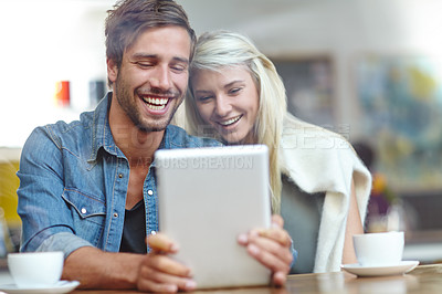 Buy stock photo Shot of a young couple laughing at someting on a tablet while on a coffee date