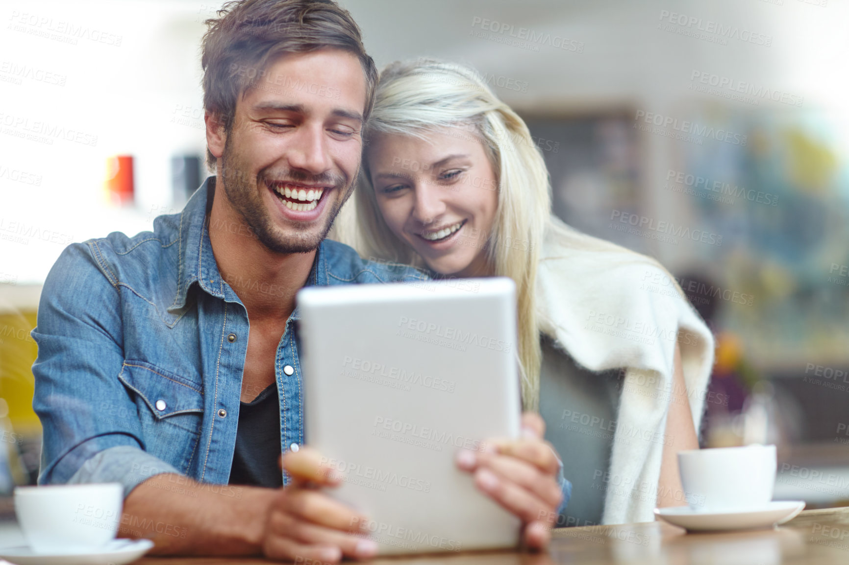 Buy stock photo Shot of a young couple laughing at someting on a tablet while on a coffee date