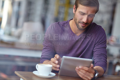 Buy stock photo Shot of a handsome young man using his tablet at a coffee shop