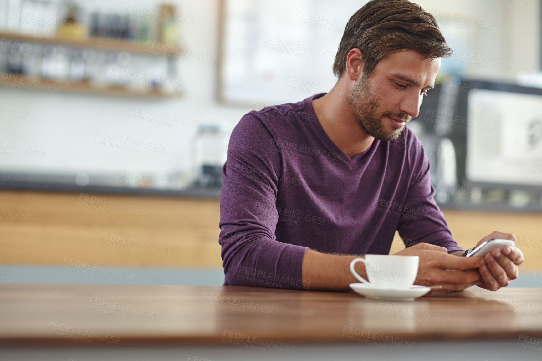 Buy stock photo Shot of a handsome young man checking his cellphone while having coffee at a cafe