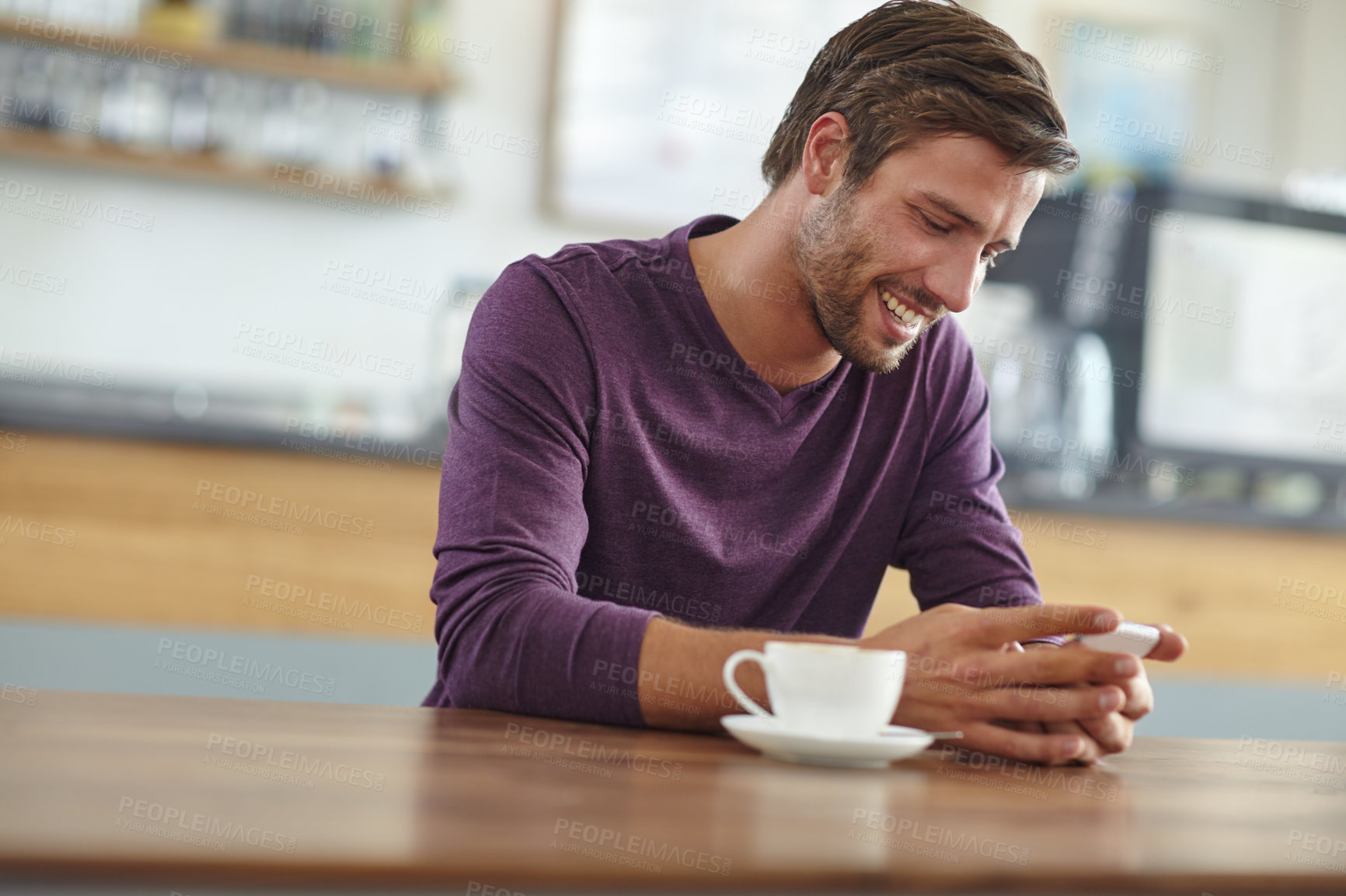 Buy stock photo Shot of a handsome young man checking his cellphone while having coffee at a cafe