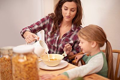 Buy stock photo Mother, girl and breakfast in house with cereal for health, nutrition and help by table. Woman, kid and brunch together in home with milk by kitchen for wellness, eating and assistance with food