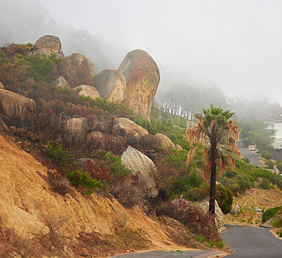 Buy stock photo Rocky landscape along a road with thick smoggy air from a wildfire spreading and destroying trees and bushes, environmental damage. Big boulders on a scenic path in Cape town on a misty morning.