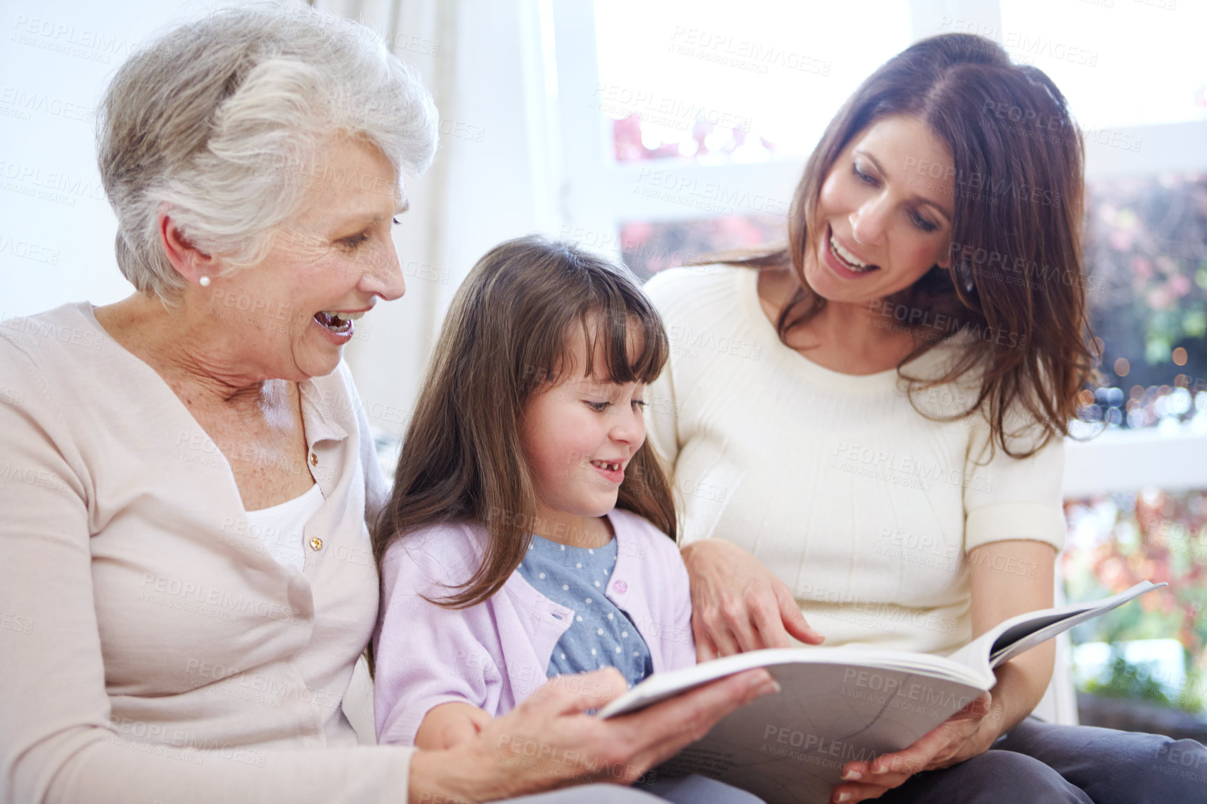 Buy stock photo Reading, book and child with mom and grandmother on sofa in living room for bonding together. Happy, relax and girl with mother and senior woman enjoying fantasy story, novel or literature at home.