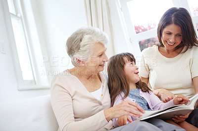 Buy stock photo Reading, book and kid with mom and grandmother on sofa in living room for bonding together. Happy, relax and girl child with mother and senior woman with fantasy story, novel or literature at home.