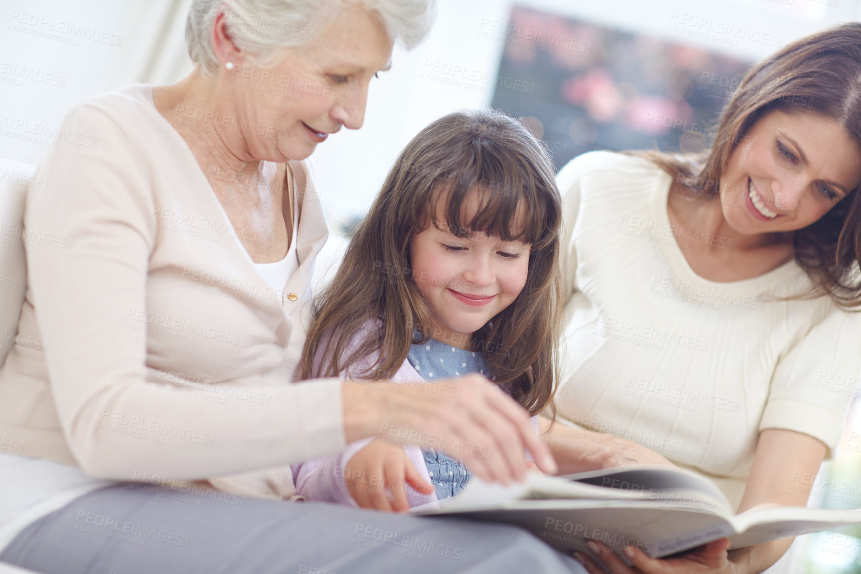 Buy stock photo Happy, book and child with mom and grandmother on sofa in living room for bonding together. Reading, relax and girl with mother and senior woman enjoying fantasy story, novel or literature at home.