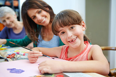 Buy stock photo Shot of a little girl painting pictures with her mother and grandmother in the background