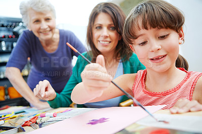 Buy stock photo Shot of a little girl painting pictures with her mother and grandmother in the background