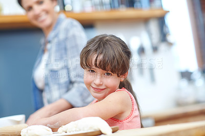 Buy stock photo A cute little girl working with cookie dough with her mother standing in the background