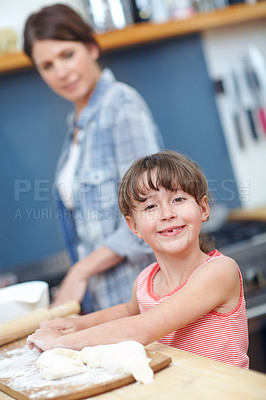 Buy stock photo A cute little girl working with cookie dough with her mother standing in the background