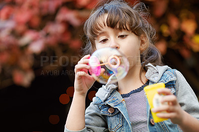Buy stock photo Shot of a little girl blowing bubbles outdoors