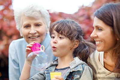 Buy stock photo Shot of a three generational family spending time outdoors blowing bubbles