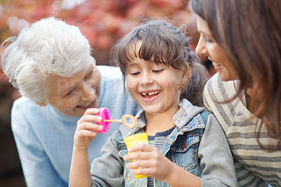 Buy stock photo Shot of a three generational family spending time outdoors blowing bubbles