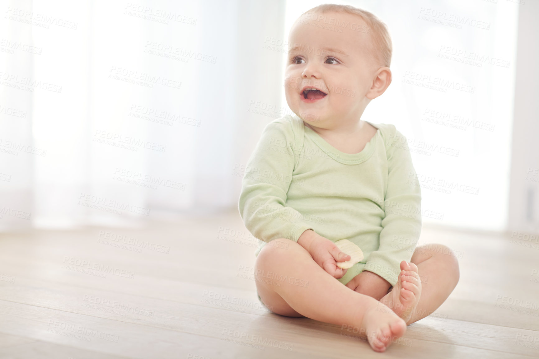 Buy stock photo Shot of a baby boy sitting on the floor while eating a snack