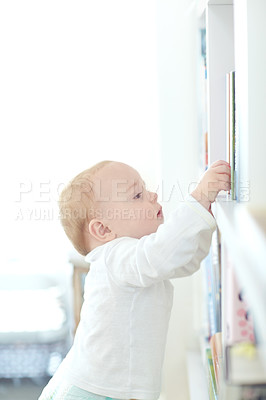 Buy stock photo Shot of an adorable baby boy standing by a bookshelf