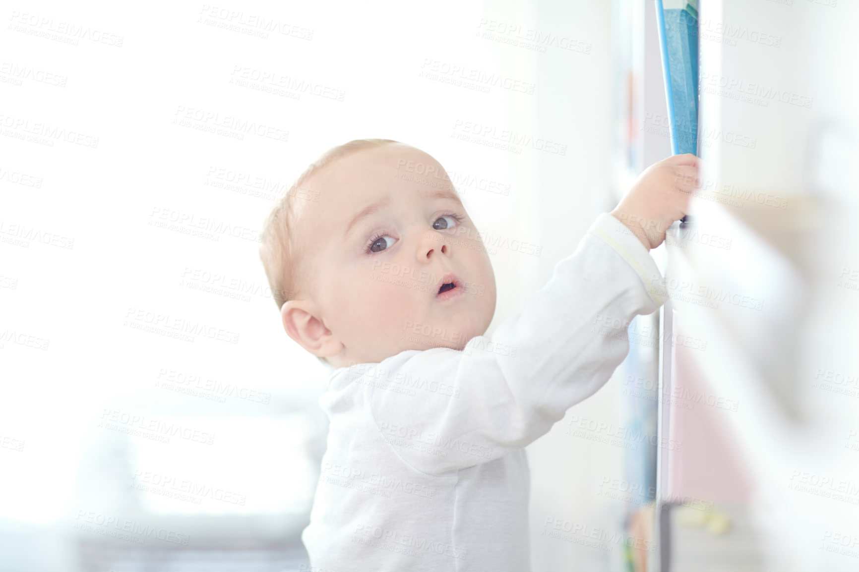 Buy stock photo Shot of an adorable baby boy standing by a bookshelf