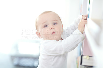 Buy stock photo Shot of an adorable baby boy standing by a bookshelf