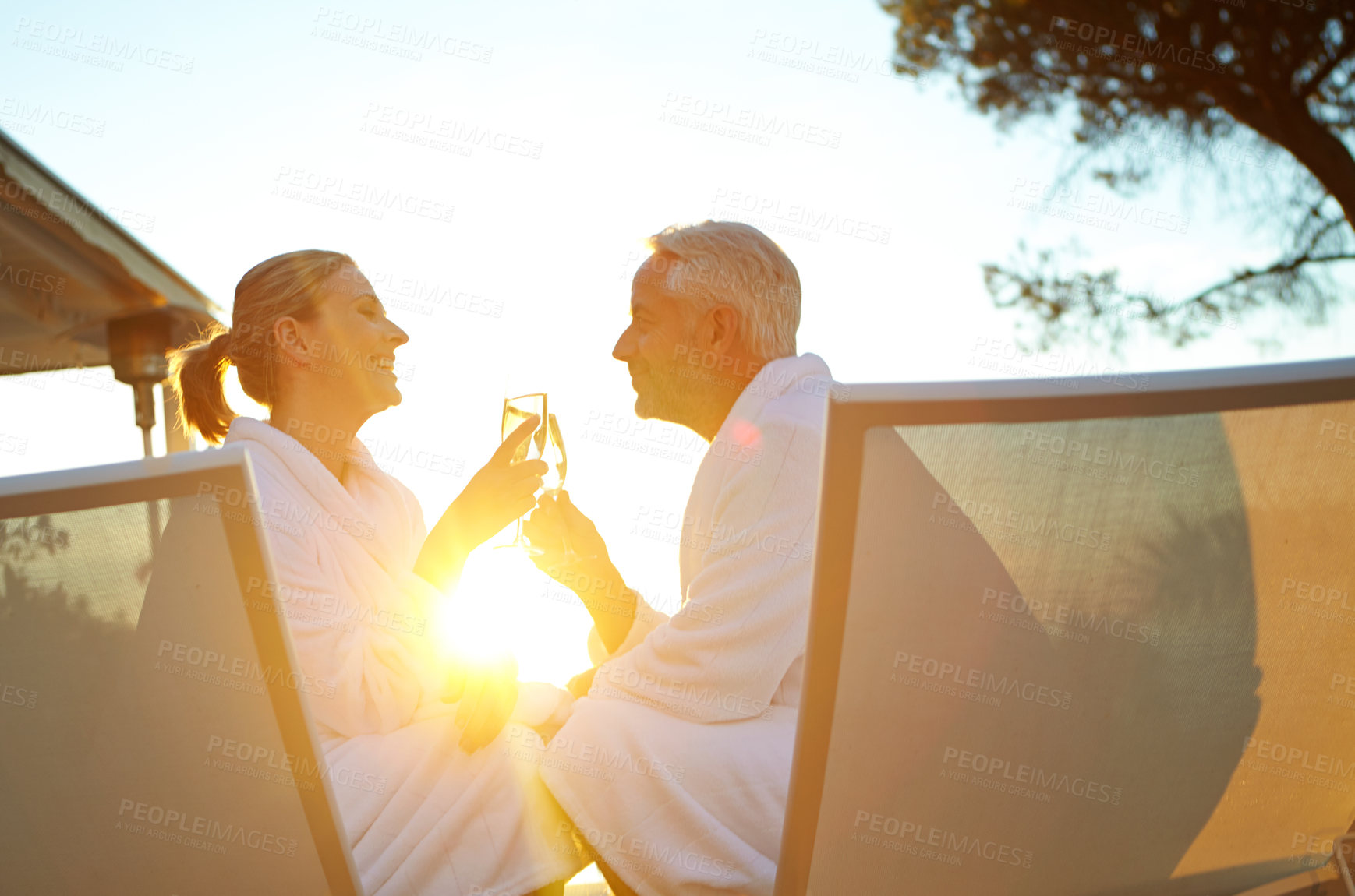 Buy stock photo Shot of a mature couple drinking champagne while relaxing in deck chairs at sunset