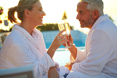 Buy stock photo Shot of a mature couple drinking champagne while relaxing in deck chairs at sunset