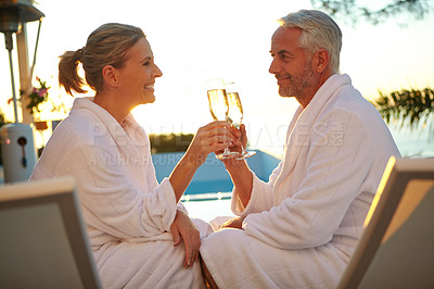 Buy stock photo Shot of a mature couple drinking champagne while relaxing in deck chairs at sunset