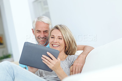 Buy stock photo Shot of a mature couple using a digital tablet while sitting on a sofa