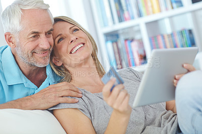 Buy stock photo Shot of a happy mature couple sitting with their tablet and doing some online shopping at home