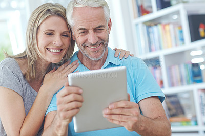 Buy stock photo Shot of a mature couple using a digital tablet while sitting on a sofa