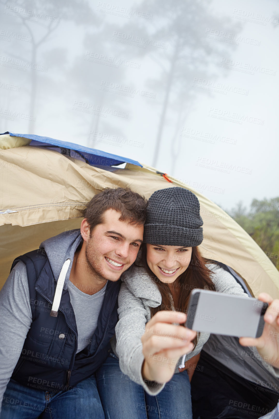 Buy stock photo Shot of a young couple taking a photo of themselves while sitting inside a tent