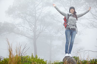 Buy stock photo Shot of a beautiful young female hiker standing on a rock with her arms outstretched