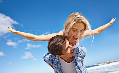 Buy stock photo Shot of a happy young couple enjoying a piggyback ride at the beach