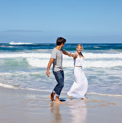 Buy stock photo Shot of a happy young couple enjoying a walk along the beach
