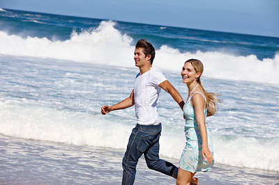Buy stock photo Shot of a happy young couple enjoying a walk along the beach