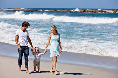 Buy stock photo Shot of a happy young family of three enjoying a walk along the beach