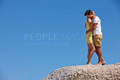 Buy stock photo Shot of a young couple enjoying an affectionate moment on top of a rock