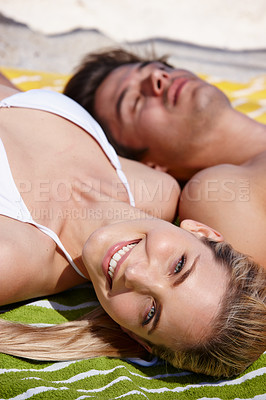 Buy stock photo Shot of a happy young couple sunbathing together at the beach