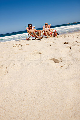 Buy stock photo Shot of a happy young couple reclining on their deck chairs at the beach