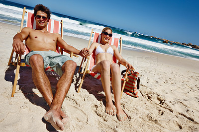 Buy stock photo Couple, smile and holding hands on beach for vacation, bonding and tropical holiday with chair. Man, woman and sunglasses outdoor for trip, love and travel with sunshine, relax or date in Maldives